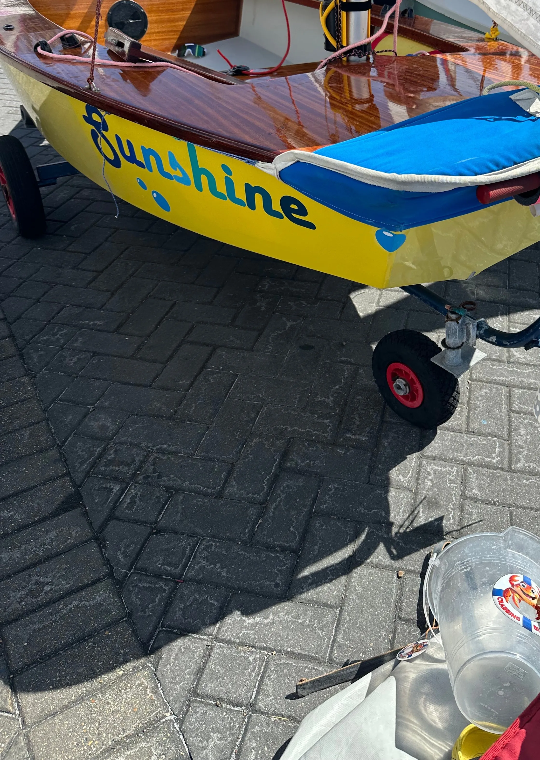 A yellow AB called Sunshine on its launching trolley in the dinghy park, varnished side decks and a blue cockpit cover, with the rest of the fleet rigged around it.