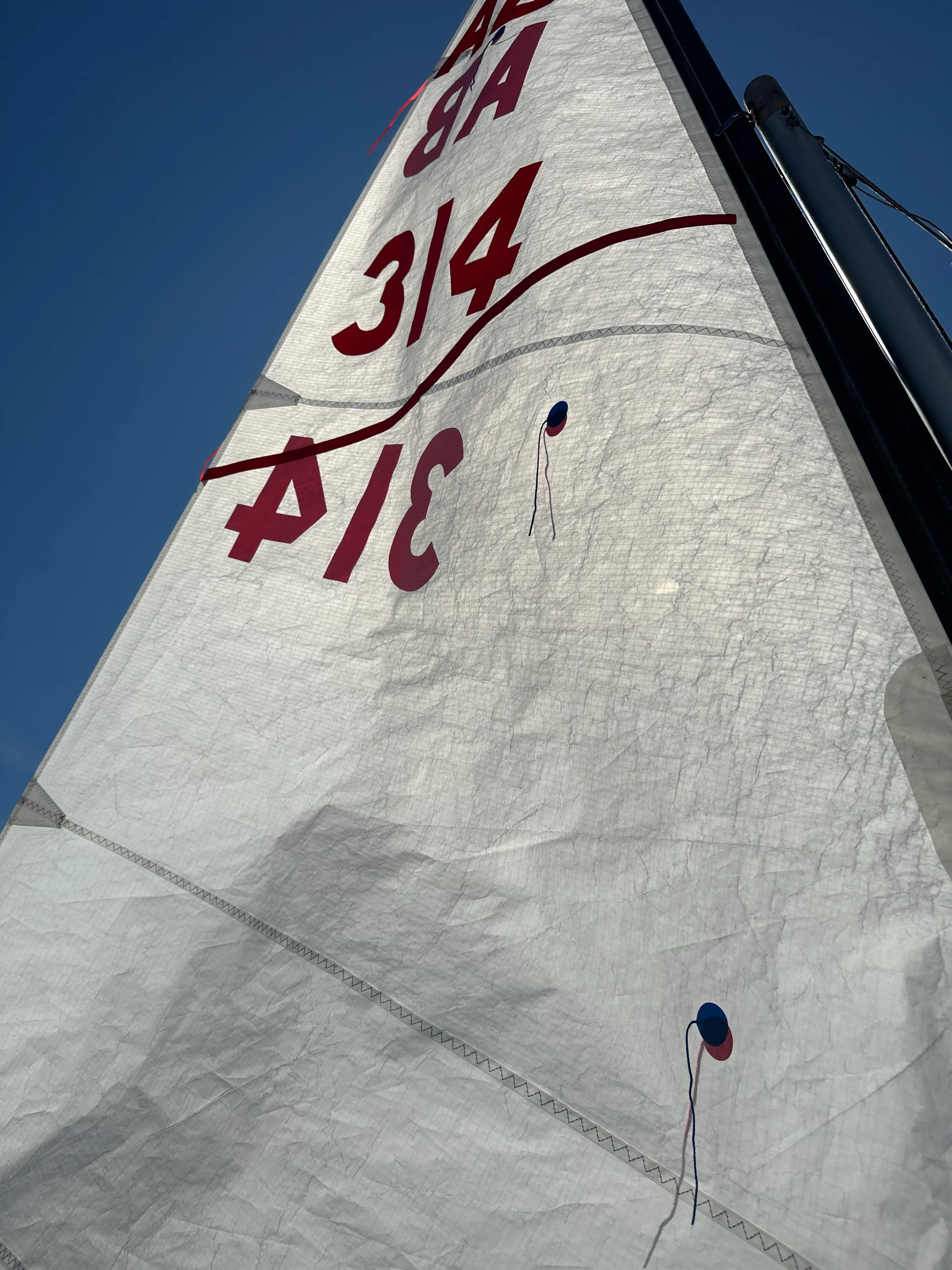 The mainsail of AB 314 seen from the cockpit against a clear sky, the sail number in red on white cloth with telltales flying.