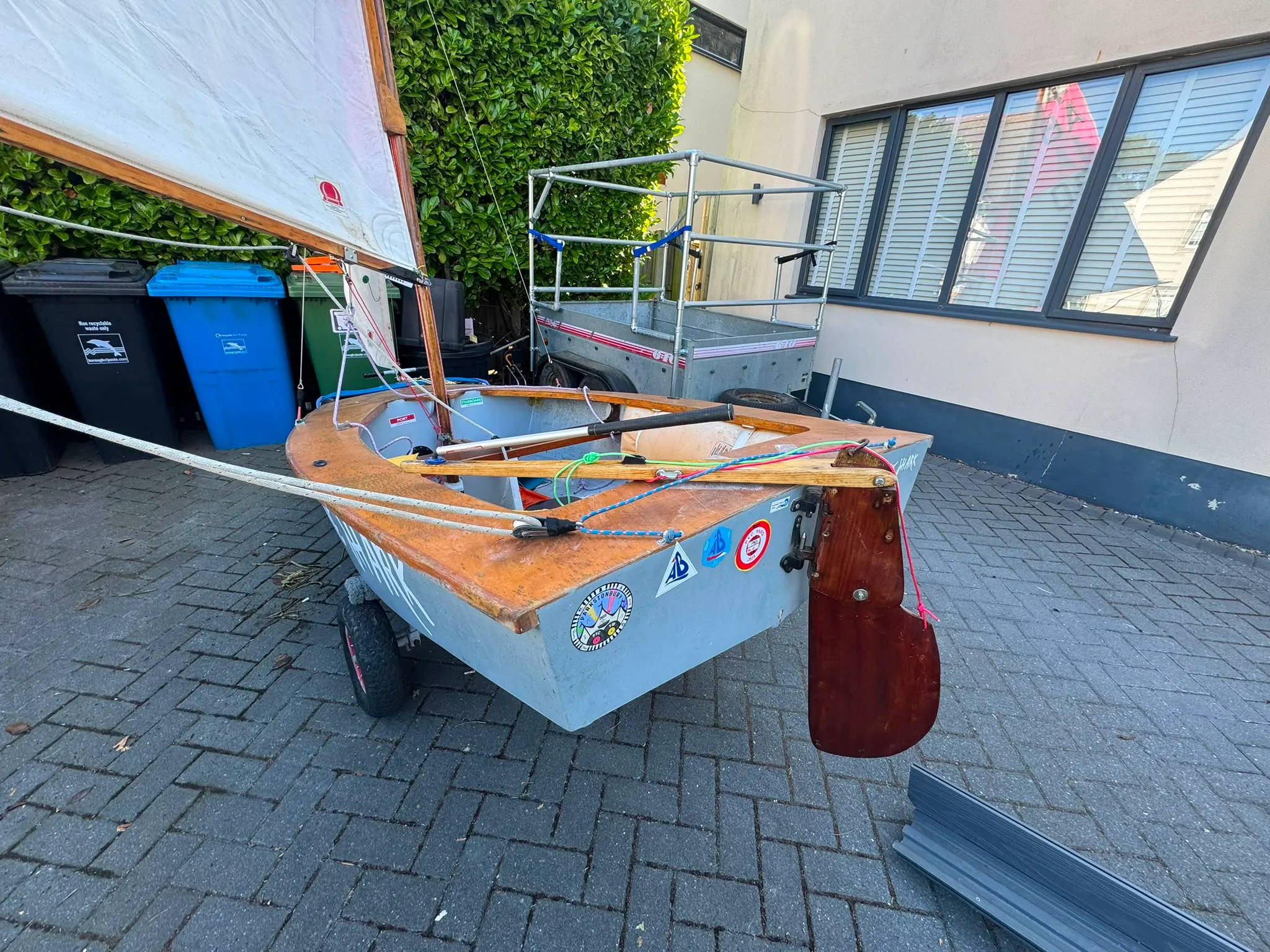 The transom close up, with club stickers, the rudder fittings, and the tiller lying across the varnished stern deck.