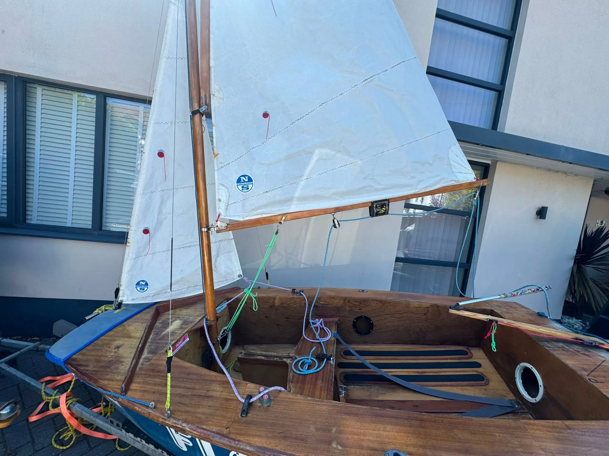 Floaty Boaty side on, the varnished wooden deck, thwart and enclosed side tanks with round inspection hatches, the floorboards with black grip strips, and the boom and sails above.