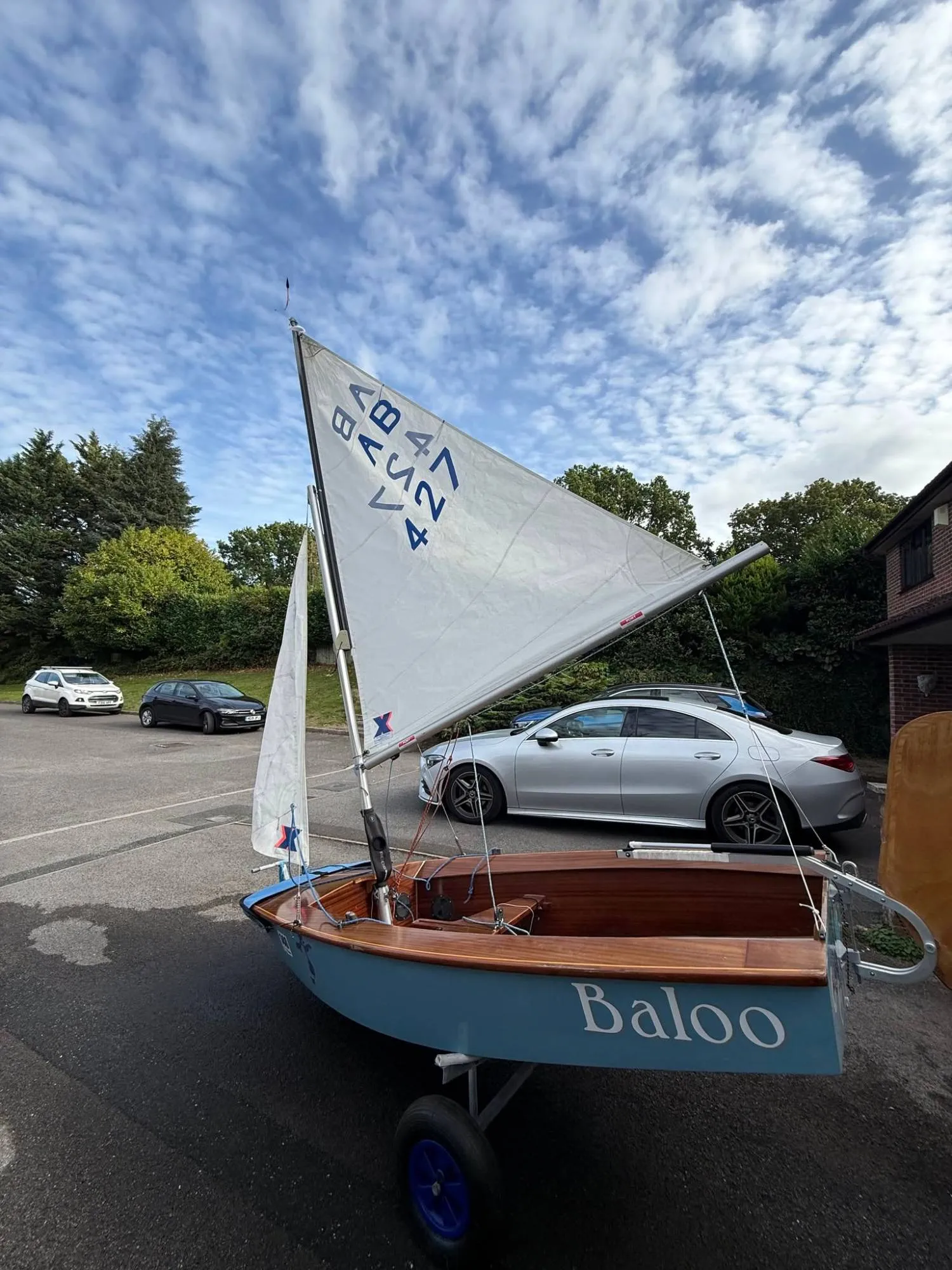 AB 427 Baloo rigged on her launching trolley, white sails with blue sail numbers, varnished wooden decks and the name Baloo on her pale blue topsides.