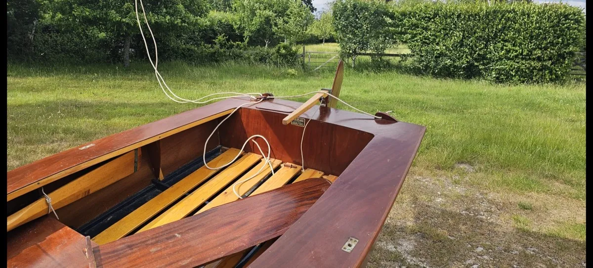 Looking down into the cockpit — original slatted floorboards, the wooden rudder stowed across the transom, and the builder’s plaque still fixed to the aft bulkhead