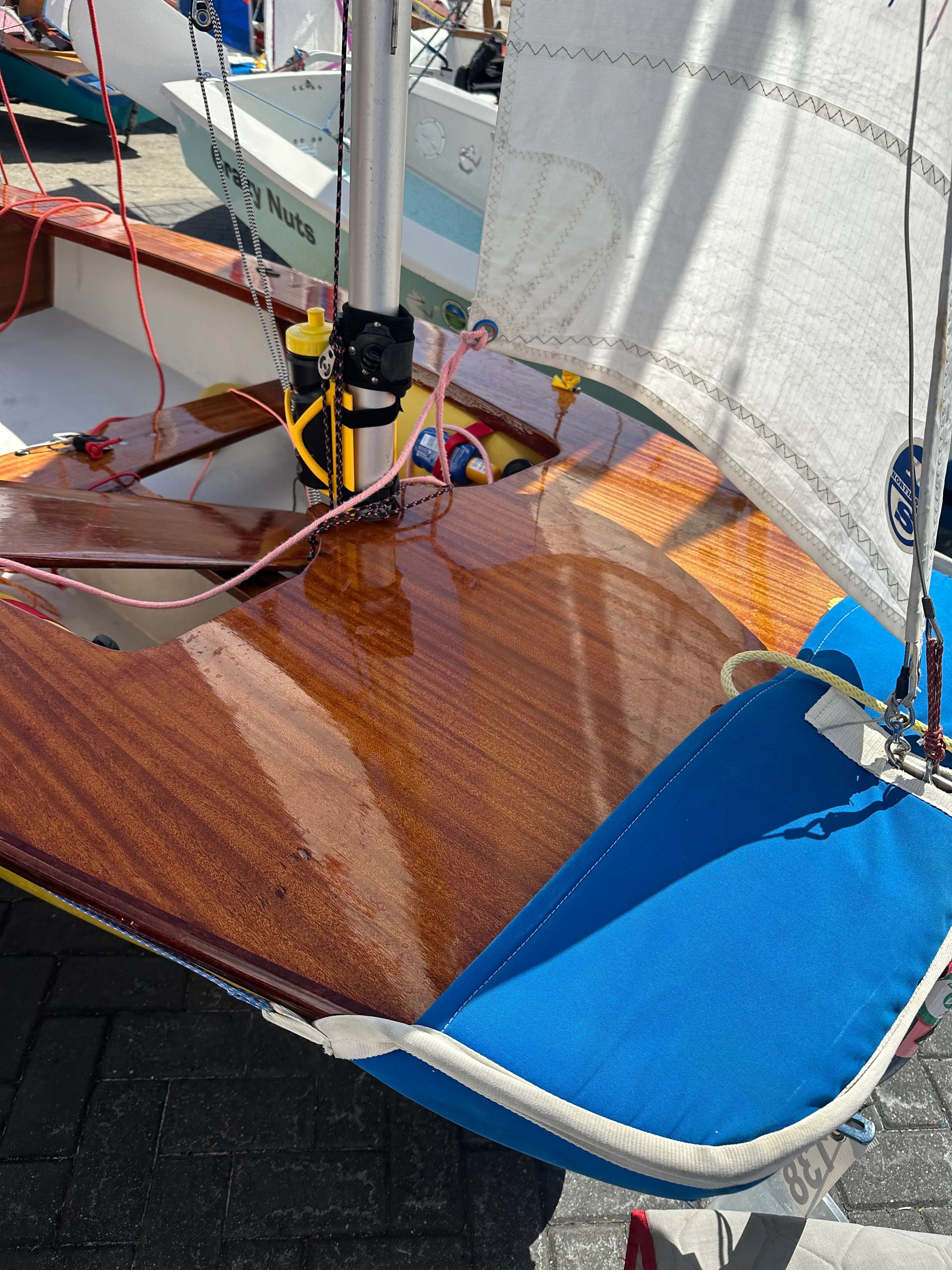 Close-up of an AB's varnished mahogany foredeck and mast, jib set and a blue cover over the side deck.