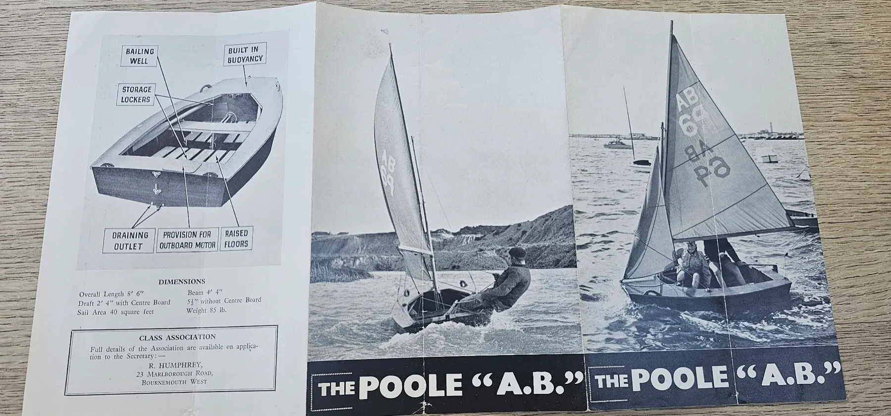 The outside of the brochure opened flat — a labelled cutaway of the hull showing bailing well, storage lockers, built-in buoyancy, raised floors, draining outlet and provision for an outboard motor, a dimensions panel, and two photographs of ABs sailing