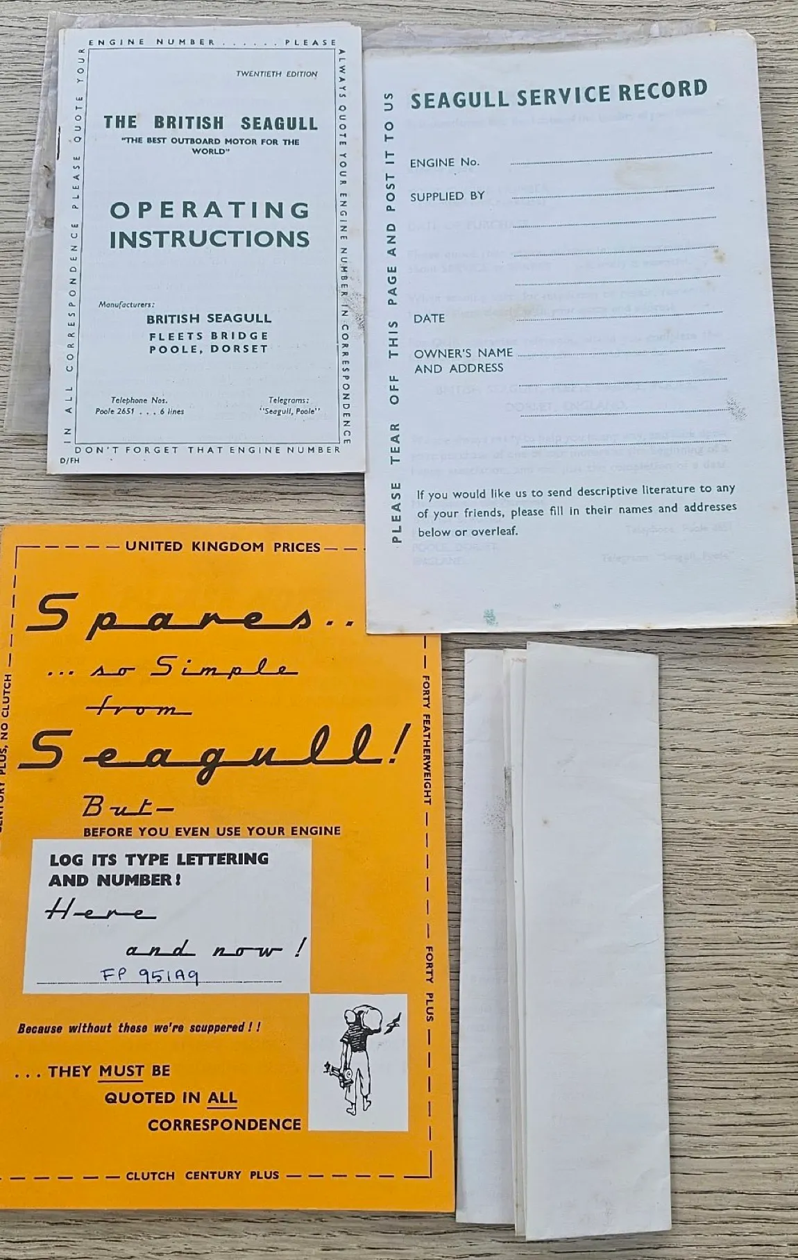 The Seagull outboard papers laid out on decking — operating instructions, a blank Seagull service record card, and an orange spares price leaflet with an engine number written on it in ink